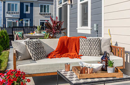 A grey couch with pillows and a blanket is on a patio.