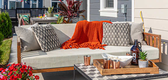 A grey couch with pillows and a blanket is on a patio.