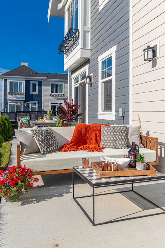 A grey couch with pillows and a blanket is on a patio.