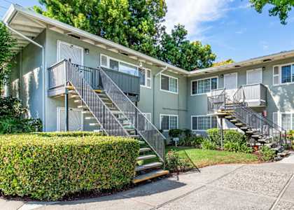 A sunny day at a two-story apartment building with a green lawn and trees.