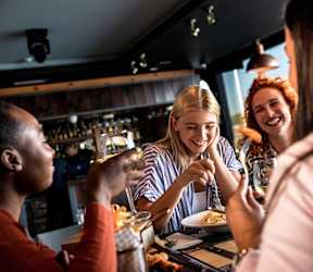 Four people are sitting at a bar, enjoying drinks and conversation.
