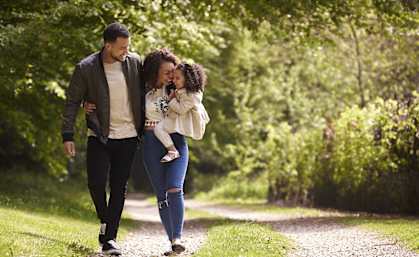 A family of three walking down a gravel road in a wooded area.