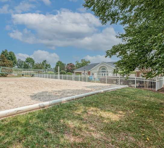 A large, empty sand pit sits in the middle of a grassy area.