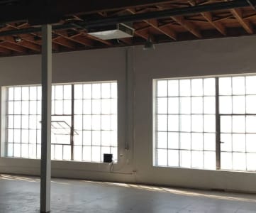an empty room with three large windows and a metal pole in the middle of the room