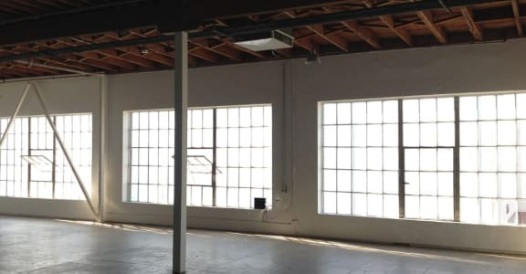 an empty room with three large windows and a metal pole in the middle of the room