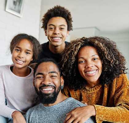A family of four is sitting closely together on a couch.