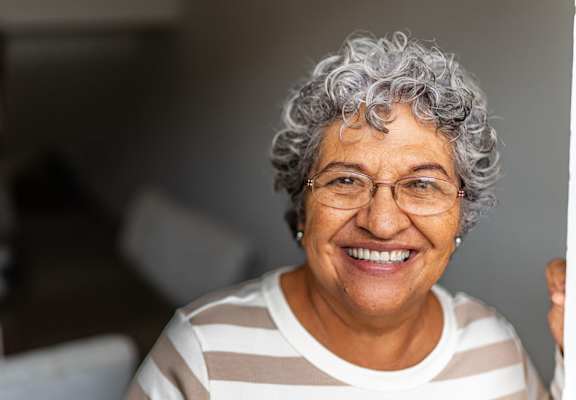 An older woman with glasses and curly hair is smiling and holding a piece of paper.
