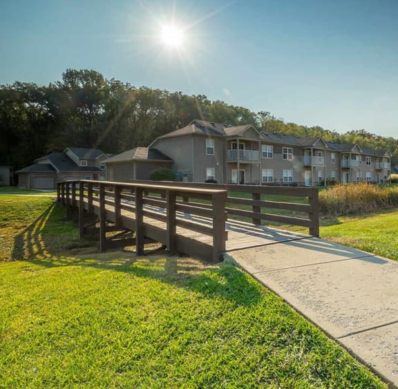 a bridge over a grassy area with apartment buildings in the background