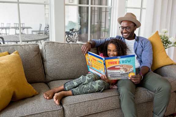 A man and a woman are sitting on a couch reading a book together.