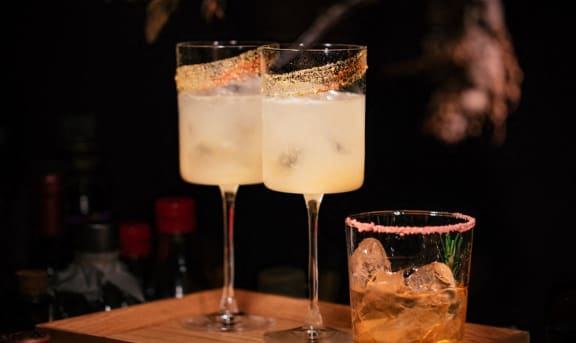 two cocktails and a glass on a wooden cutting board