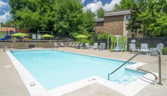 a swimming pool with chaise lounge chairs and umbrellas in front of a brick building at Stonewater Apartments, Louisville, KY 40241