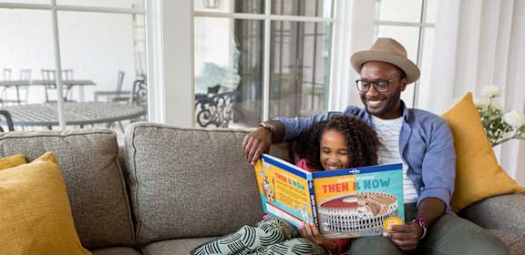 A man and a young girl are sitting on a couch reading a book together.