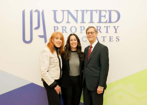 Three people pose in front of a United Property Coates sign.