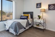 A bedroom with a bed, nightstand, and a window with blinds. at Three Crown Apartments, California, 94501