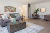 A living room with a grey couch, a coffee table, and a large painting on the wall. at Three Crown Apartments, California, 94501