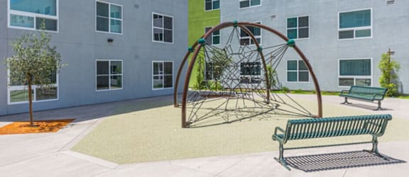 A playground with a swing set and two benches in front of a building.