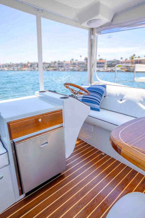A boat's galley with a stainless steel refrigerator and wooden flooring.