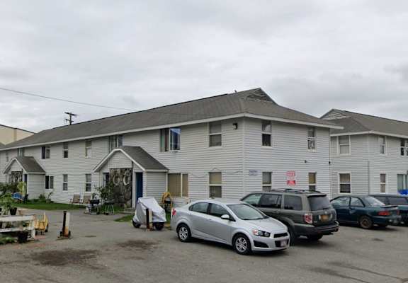 A grey car is parked in front of a white building.