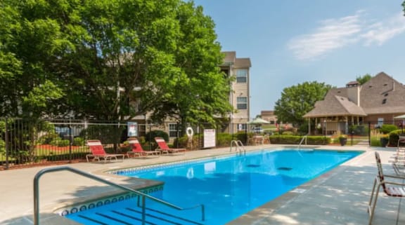 A swimming pool surrounded by trees and chairs.