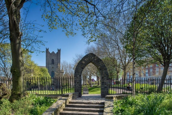a stone arch in a park with a church in the background