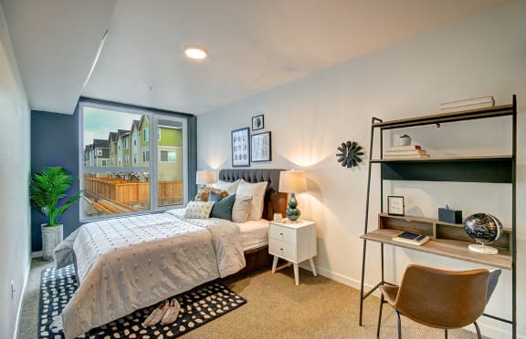 One Bedroom Apartments in West Seattle WA - Upton Flats - Spacious Bedroom wtih Carpetted Floor, Bed, Nightstands with Lamps, Desk, Large Window, and House Plant