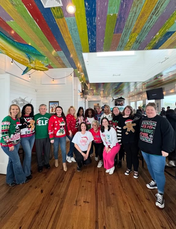 A group of people wearing Christmas sweaters are posing for a photo.