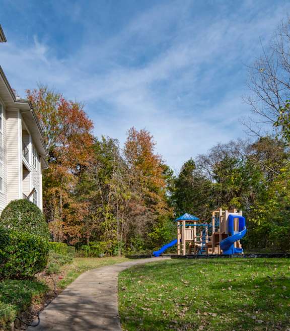 A playground with a blue slide is located in front of a white building.