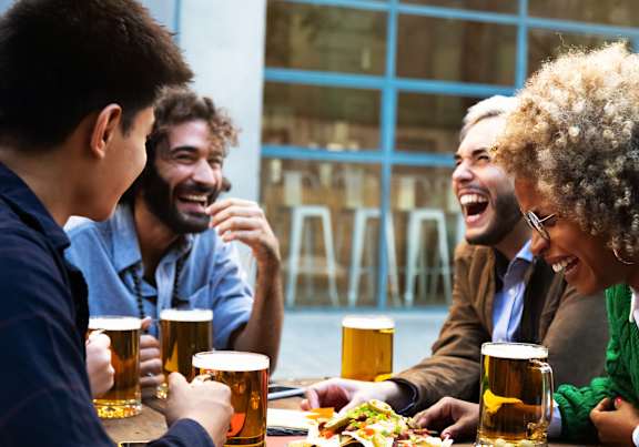 Four people laughing and drinking beer at a table.