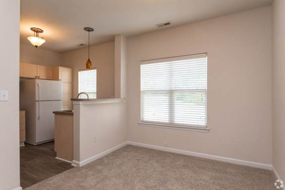 A kitchen area with a refrigerator, cabinets, and a window with blinds.