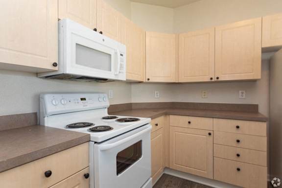 A white microwave oven is mounted above a white stove in a kitchen.
