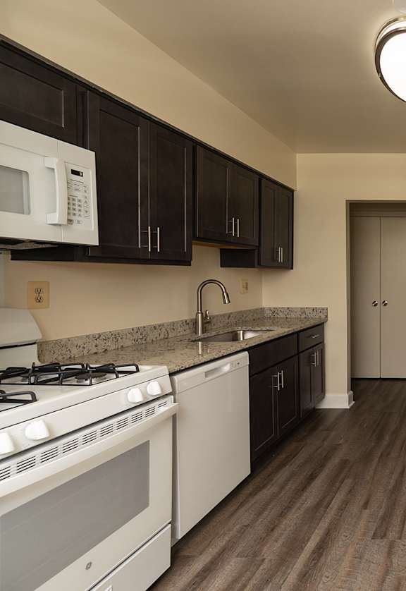 A kitchen with white appliances and dark brown cabinets.