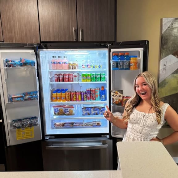 A woman is standing in front of an open refrigerator filled with various food items.