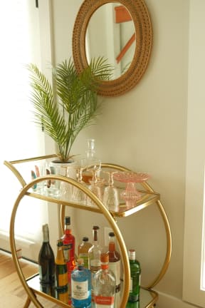 a gold bar cart with a plant on top of it and a mirror on the wall above