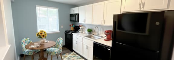 A kitchen with a black refrigerator and white cabinets. at Highview Manor Apartments, Fairport