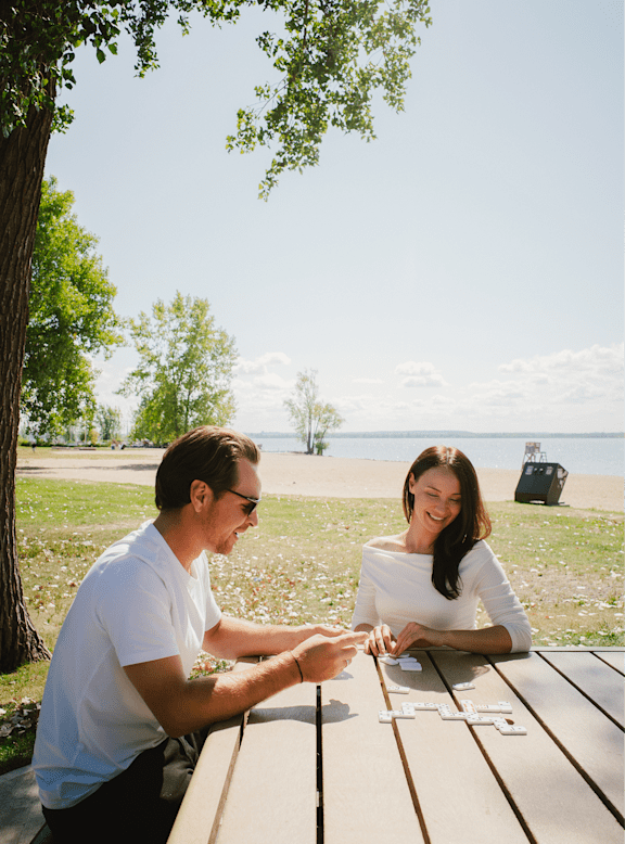 A man and a woman are sitting at a picnic table playing a game with letter tiles.