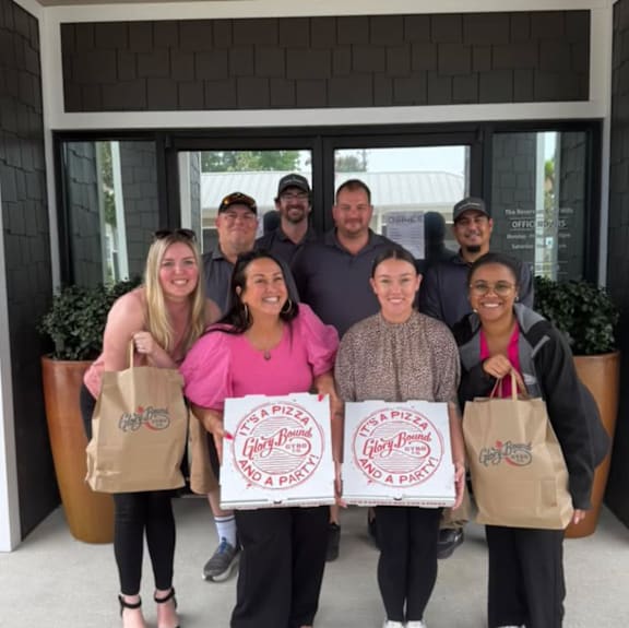 A group of people holding Es Pizza and a party signs in front of a building.