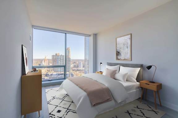 A bedroom with a large bed and a city view through the window.