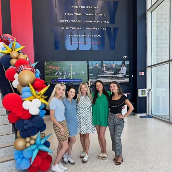 Four women are standing in front of a movie poster.