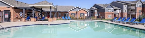 A large swimming pool in front of a building with lounge chairs around it.
