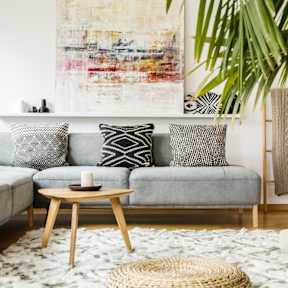 A living room with a grey couch, a wooden coffee table, and a large abstract painting on the wall.