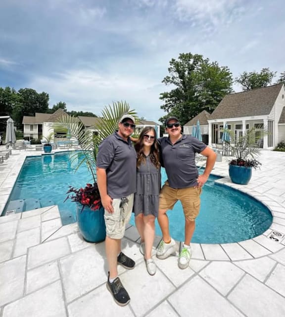 Three people stand by a pool on a sunny day.