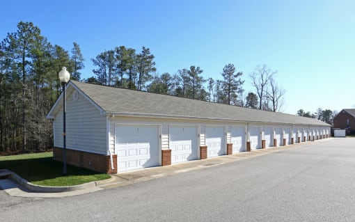 a row of garages with white doors and a street at Chester Village Green Apartments, Chester, VA, 23831