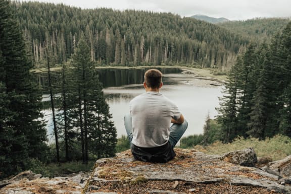 Man Sitting on Rock Admiring View of Lake and Mountains