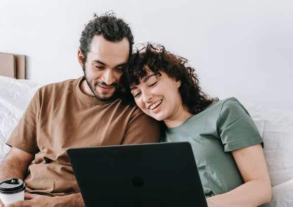 a man and a woman sitting on a bed looking at a laptop computer