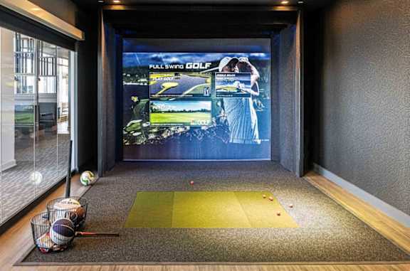 A room with a screen showing a golf game and golf balls on the floor.