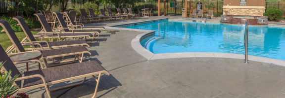 a swimming pool with chaise lounge chairs and umbrellas  at Stonepost Lakeside Apartments , Kansas , 66103