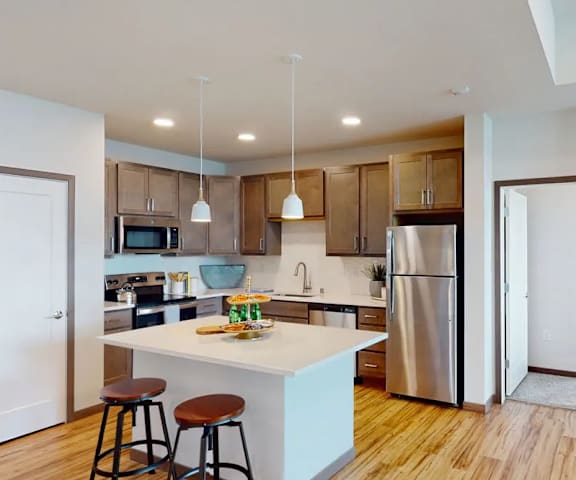 A large, modern kitchen with stainless steel appliances, overhead lighting, white marble countertops with lots of room, decorations, and large medium wooden cabinets at Van Buren West Apartment Homes.