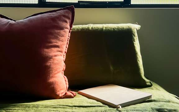 A book is placed on a bed with a red pillow and a green pillow beside it.