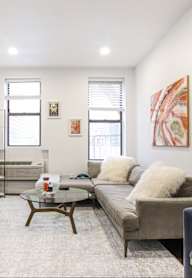 A living room with a grey couch, a white vase, a red chair, and a painting on the wall.