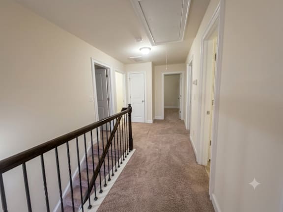 A long hallway with a carpeted floor and a railing on the left side.